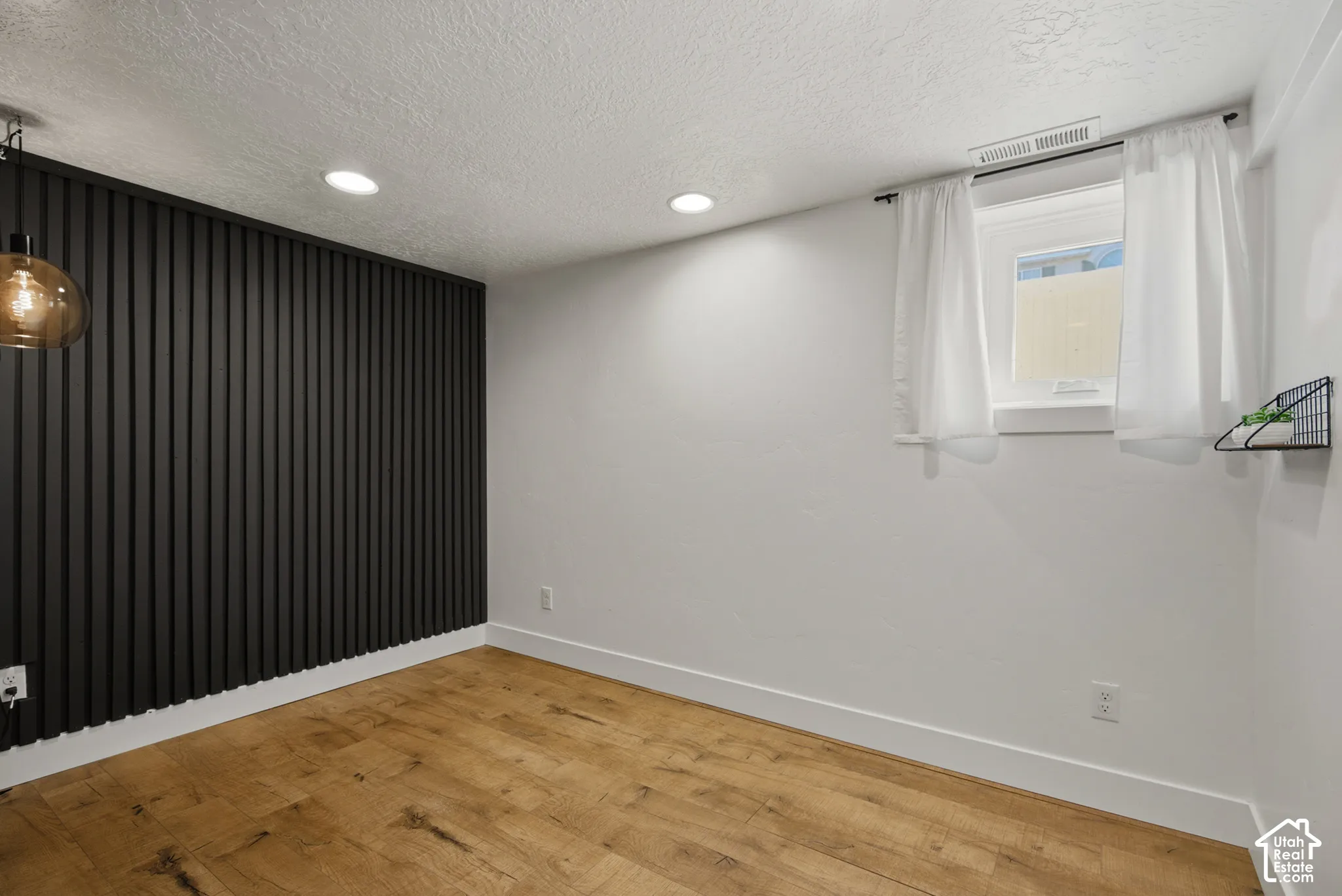 Accent wall with vertical paneling, recessed ceiling lighting, wood-finish flooring, and a single window