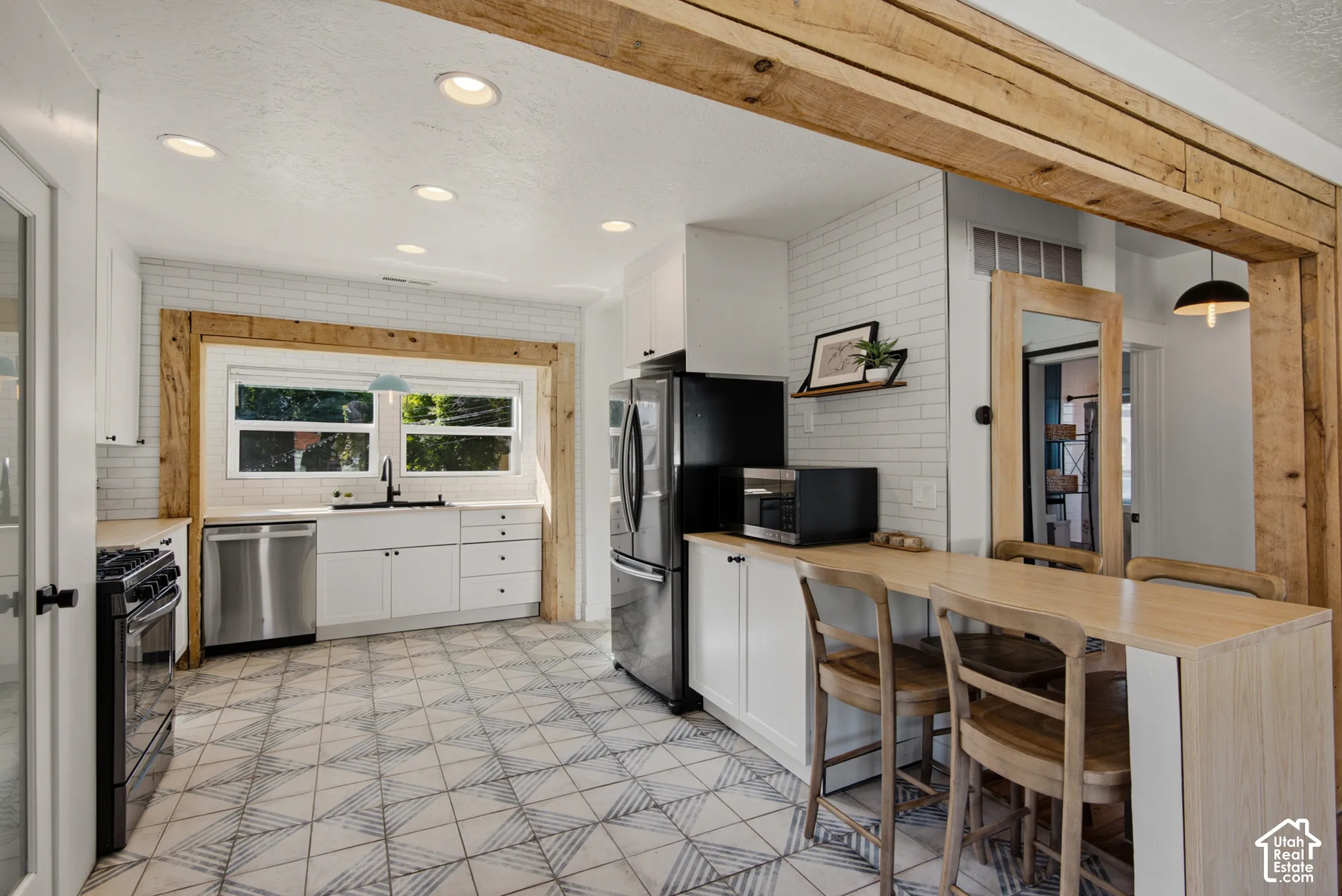 Kitchen featuring wood-finish flooring, white subway tile backsplash, white cabinetry, and stainless steel appliances