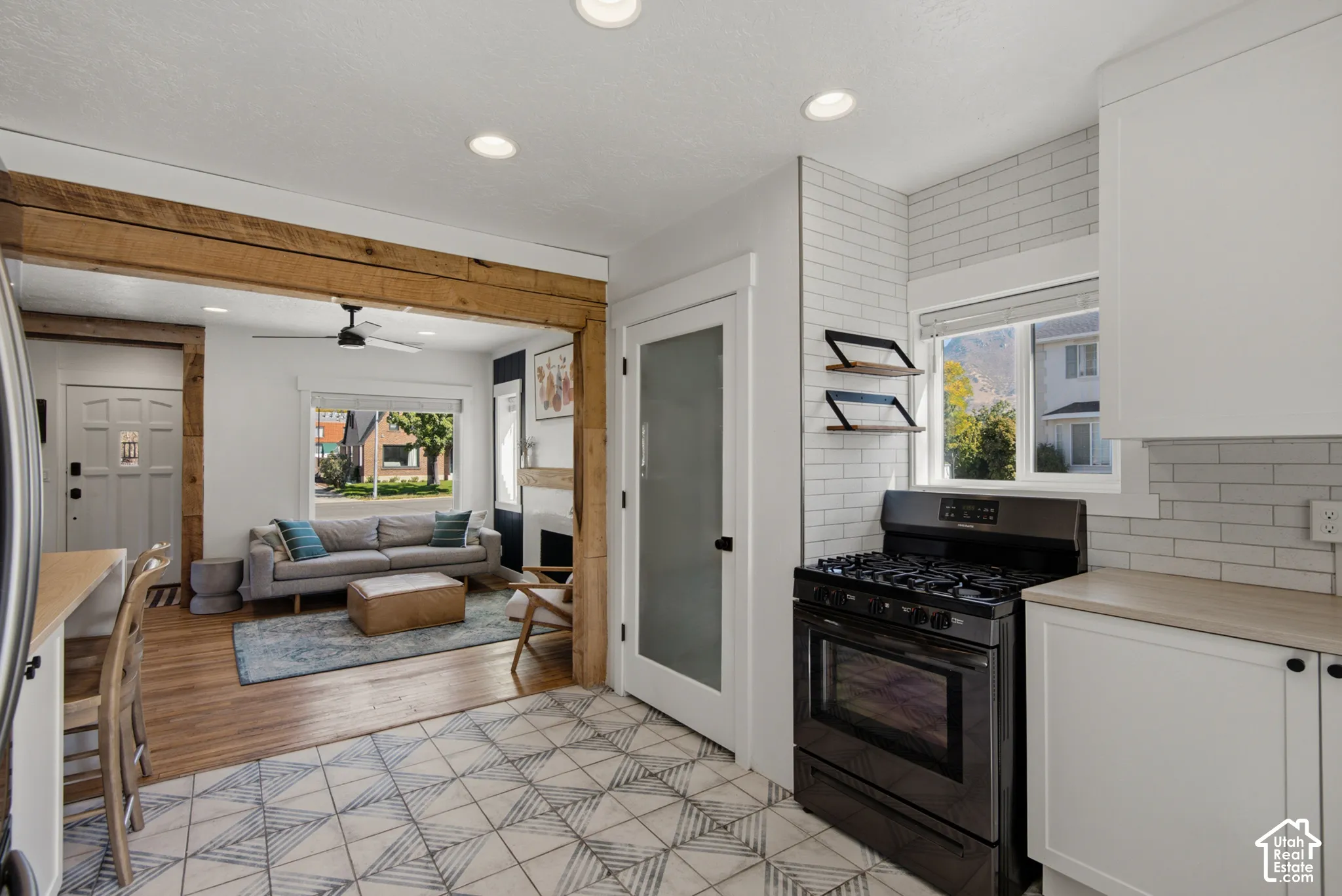 Kitchen featuring patterned tile flooring, white subway tile backsplash, white cabinetry, and a black range