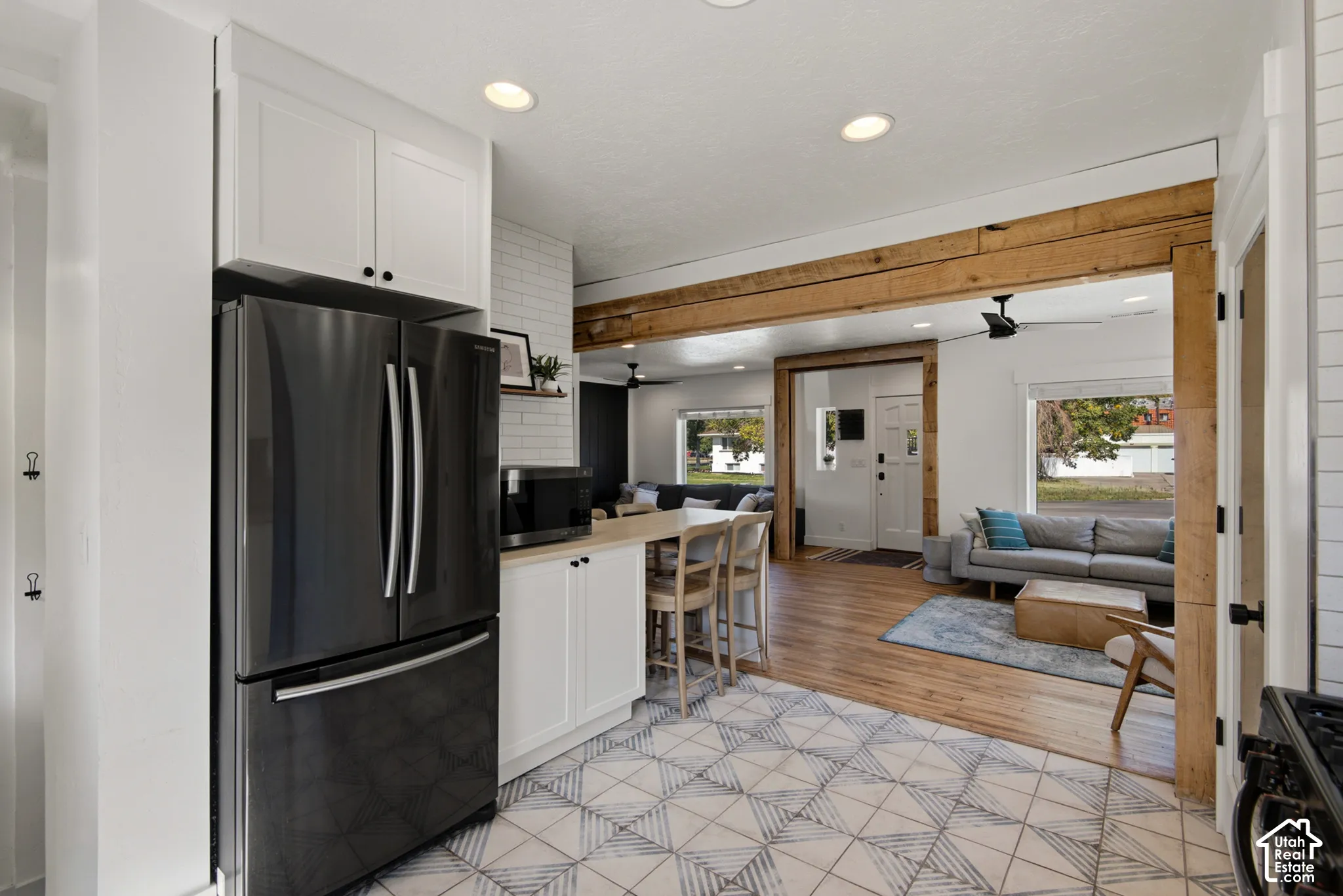 White shaker cabinetry, dark stainless steel refrigerator, patterned floor tile, wood beam accents, and wood-finish flooring