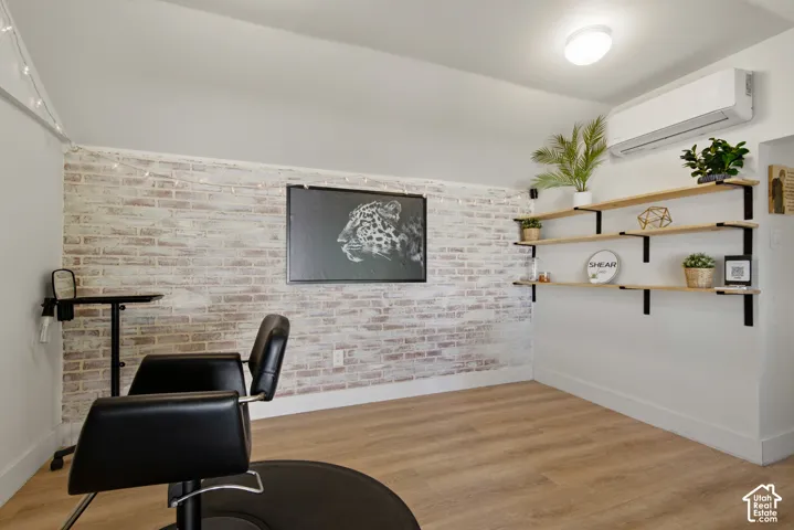 Painted brick accent wall, wood-finish flooring, built-in wall shelving, ceiling-mounted lighting, and a wall-mounted climate control unit