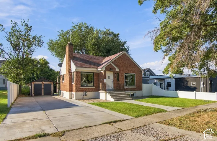 Brick exterior with a prominent chimney, concrete driveway, detached two-car garage, and a manicured lawn