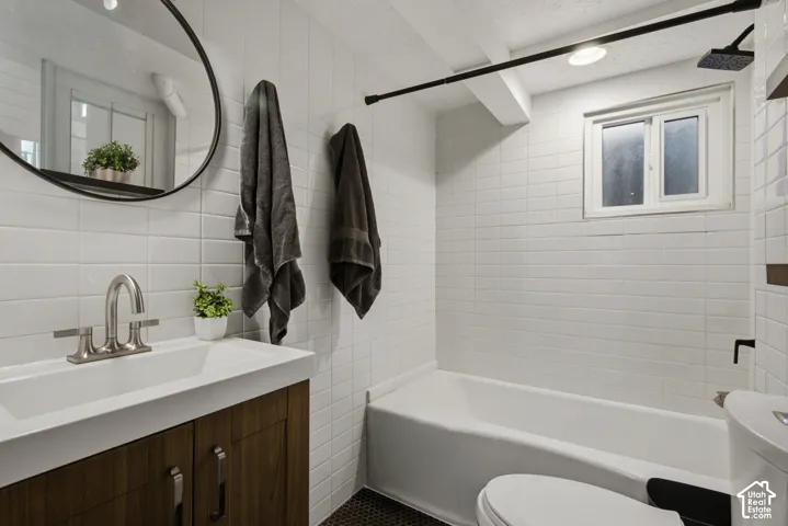 White subway tile walls, wood-finish vanity with integrated sink, brushed nickel faucet, deep soaking tub, and black hexagonal floor tiles