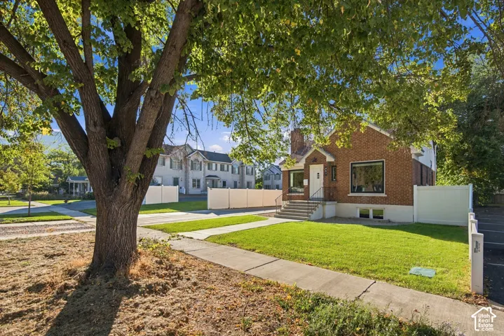 Brick exterior, manicured lawn, front sidewalk, white privacy fencing, and mature trees