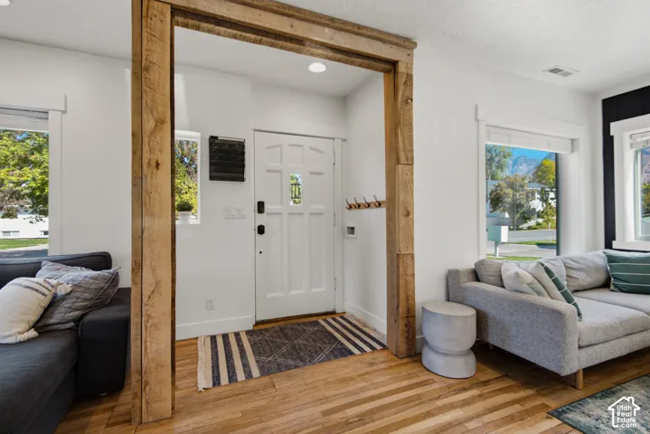 Hardwood flooring throughout, a rustic wood-beam doorway, white paneled entry door with transom detailing, and recessed lighting