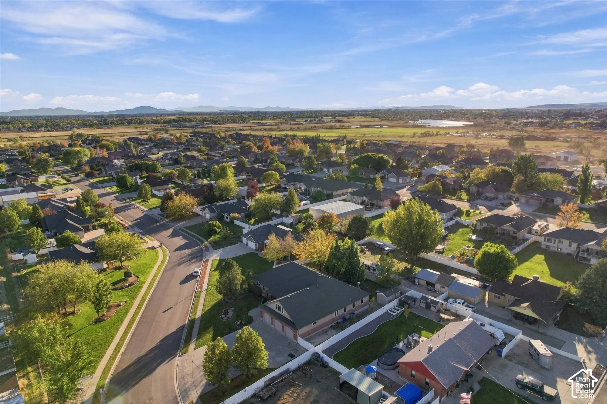 Aerial perspective featuring a residential lot with a fenced backyard, hardscaped patio area, multi-car garage, and distant mountain backdrops
