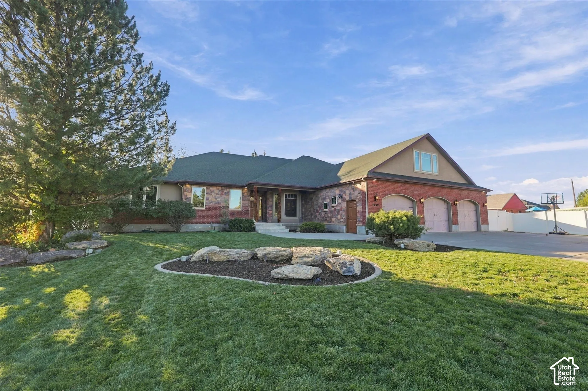 Exterior featuring a brick and stone facade, multi-gabled roofline, three-car garage, and landscaped lawn with stone hardscaping