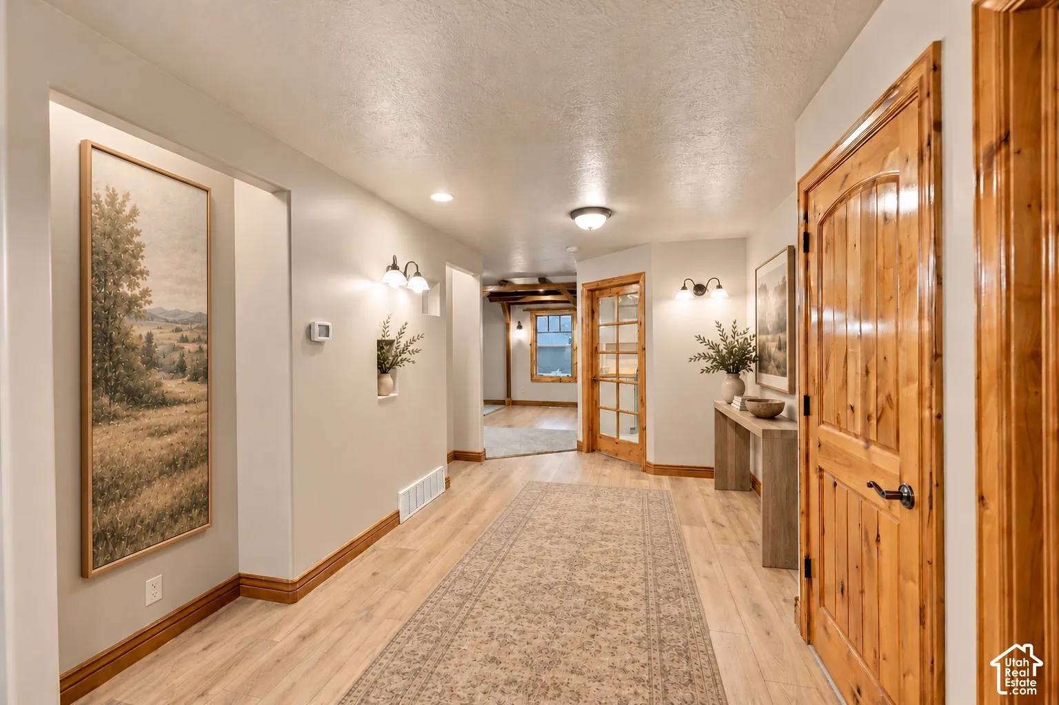 Interior hallway featuring wood-finish flooring, natural-finish wood door trim, recessed lighting, wall-mounted sconces, and built-in wall niches