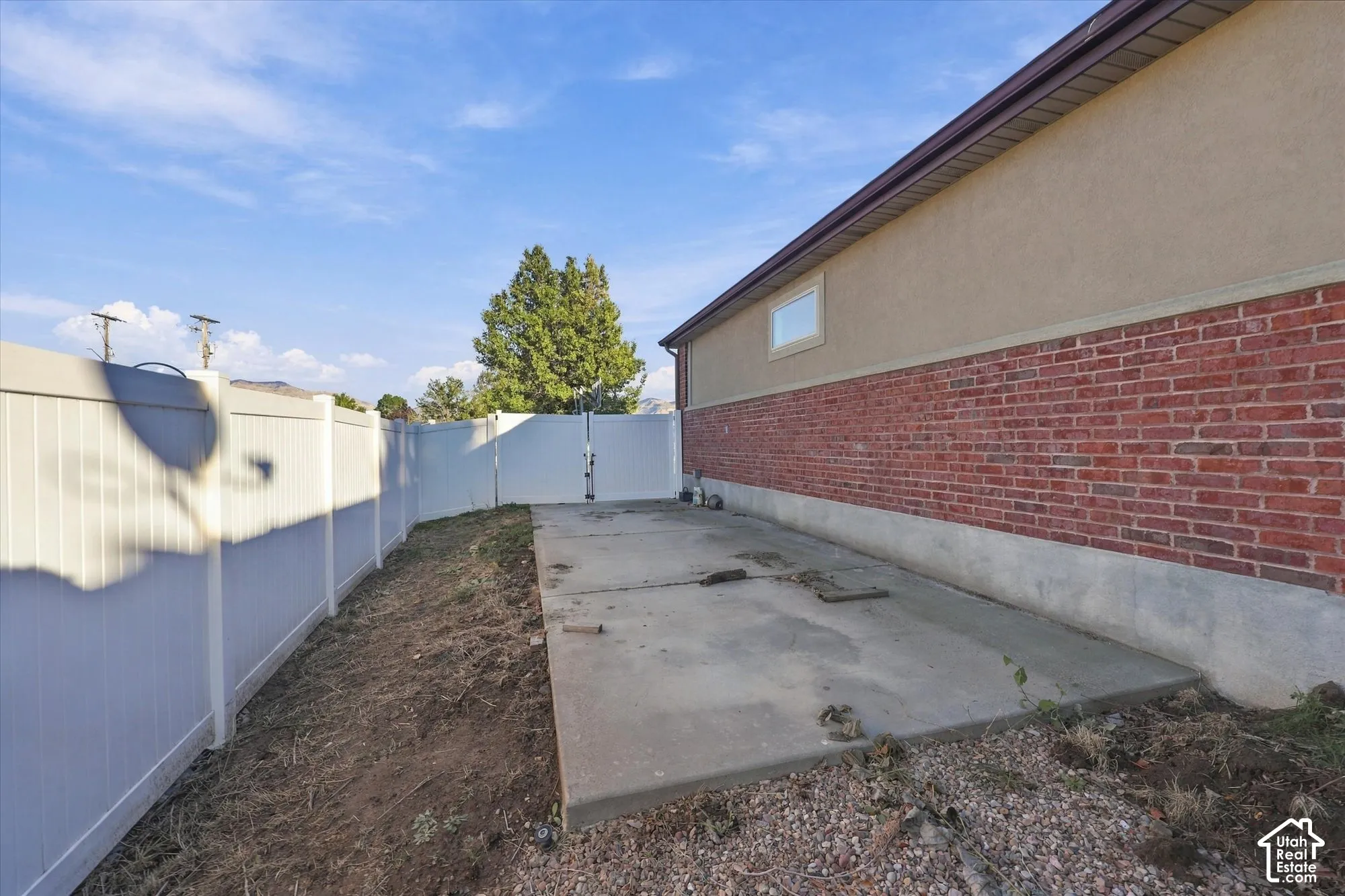 Concrete side patio featuring a red brick and stucco exterior, enclosed by full-height vinyl privacy fencing with a double-gate entry