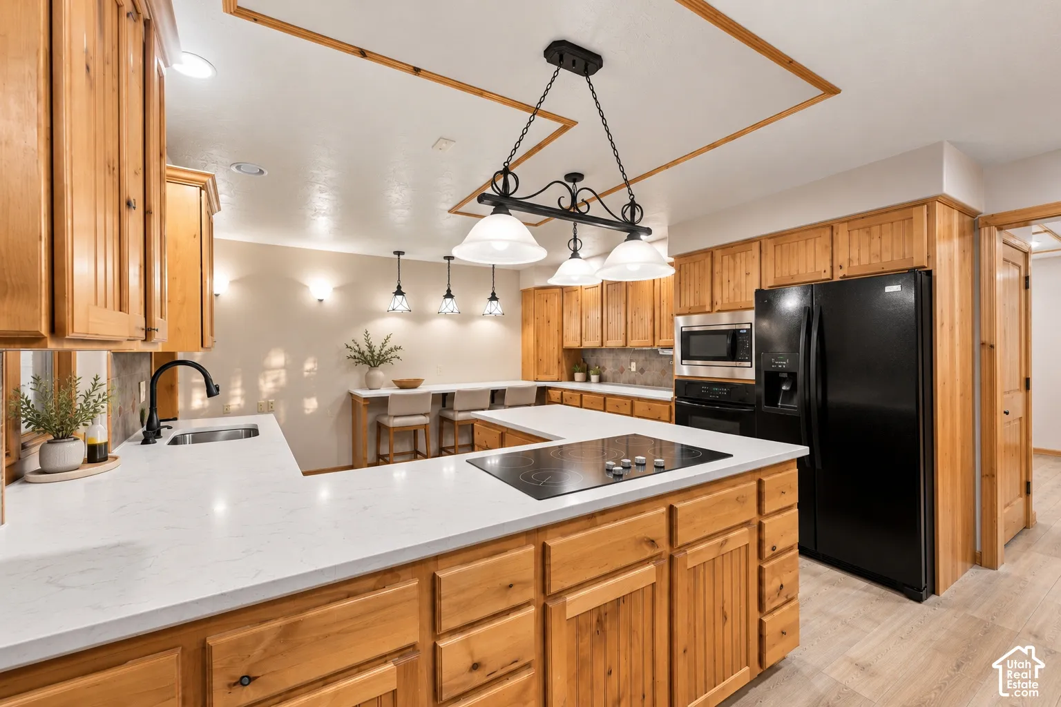 Kitchen featuring natural wood cabinetry, white stone-surface countertops, an integrated cooktop, a multi-light fixture over the island, and wood-finish flooring