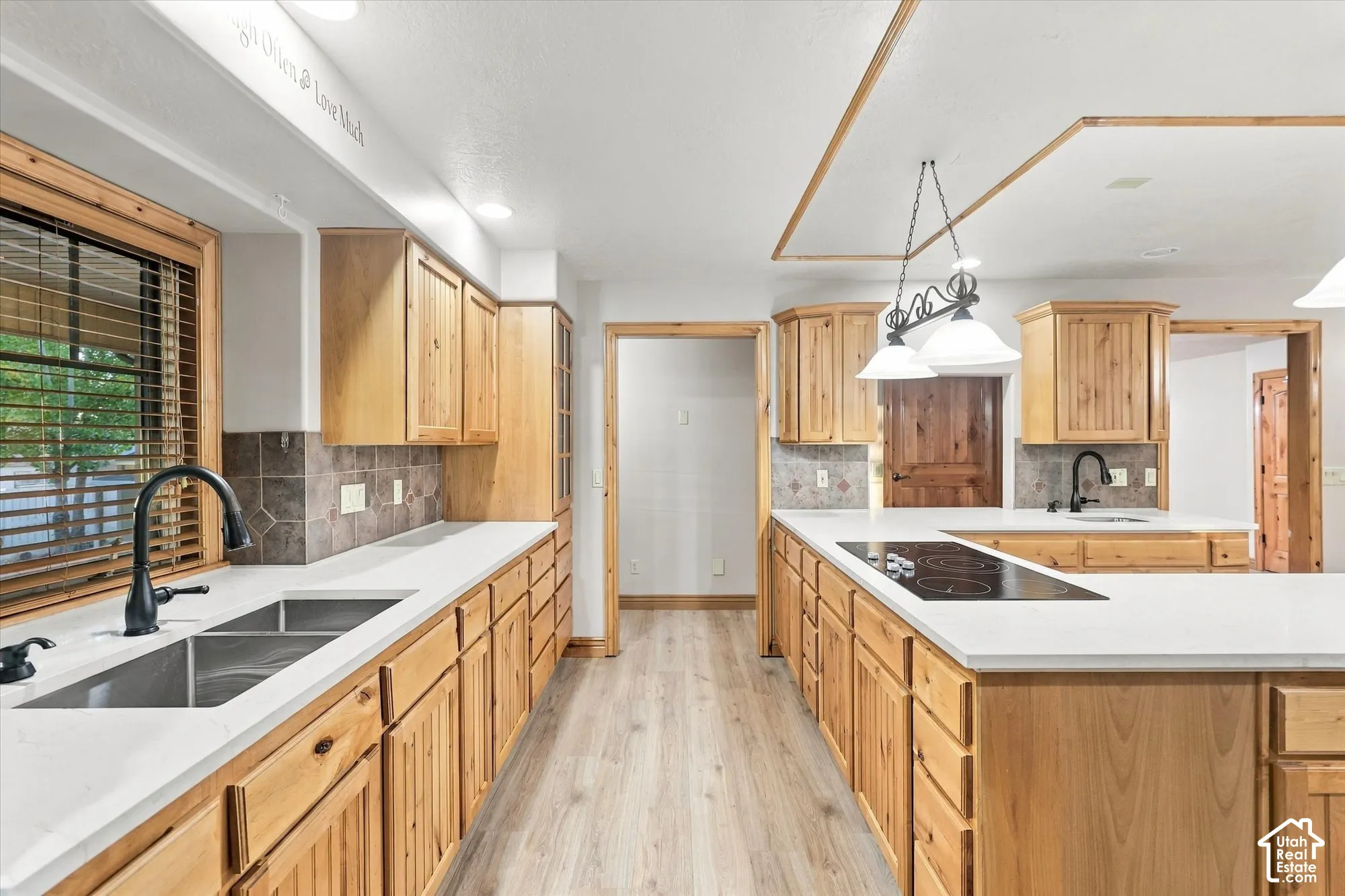 Kitchen featuring light wood cabinetry, quartz countertops, a dual-basin undermount sink with a matte black faucet, and wood-finish flooring
