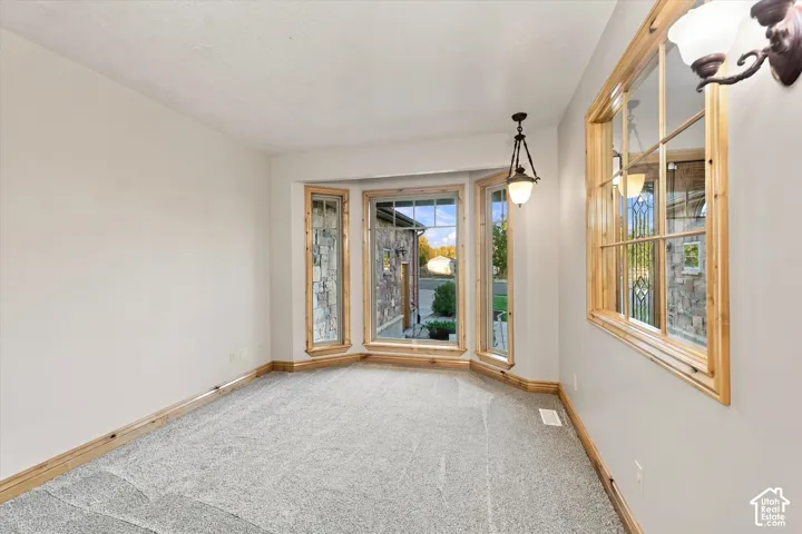 Bay window featuring natural wood trim, wall-mounted light fixtures, and neutral carpeting
