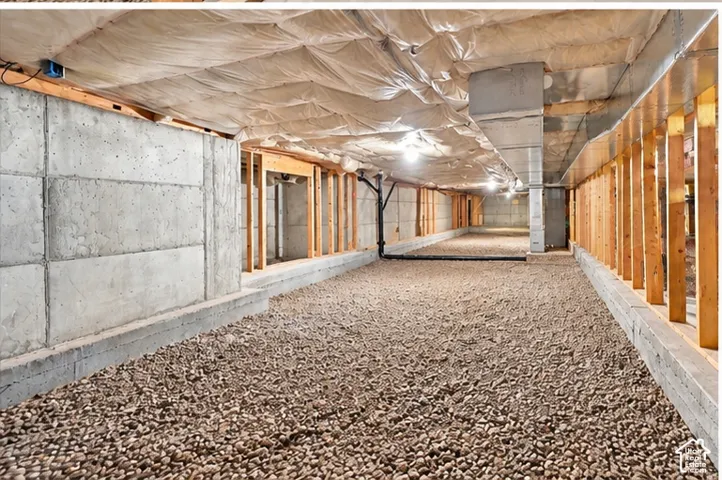 Unfinished crawl space featuring poured concrete foundation walls, stone gravel ground cover, insulated ceiling joists, and exposed wood framing