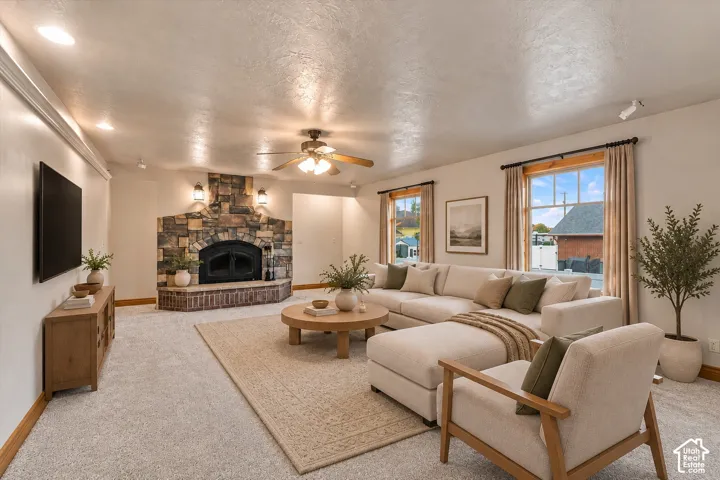 Living area featuring a floor-to-ceiling stone fireplace, raised masonry hearth, recessed lighting, ceiling fan, and large windows with wood trim