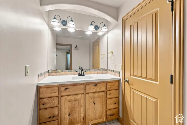 Vanity featuring natural-finish wood cabinetry, a solid-surface countertop with an integrated rectangular sink, a multi-light wall fixture, and a recessed arch architectural detail
