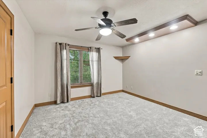 Room featuring carpeted flooring, a ceiling fan with integrated lighting, a built-in wooden soffit with recessed lighting, and a corner mounted shelf