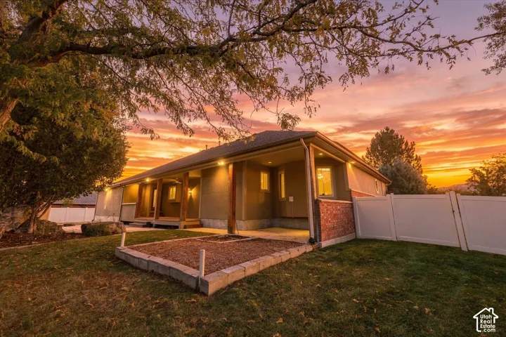 Stucco and brick exterior featuring a covered patio, raised stone-bordered landscaping bed, and white vinyl perimeter fencing