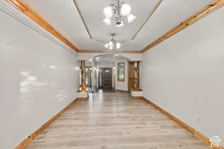 Interior space featuring wood-finish flooring, natural wood crown molding, a tray ceiling with dual multi-arm chandeliers, and decorative wood pillars