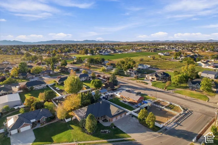 Aerial perspective featuring a multi-gabled roofline, three-car garage, concrete driveway, and white vinyl perimeter fencing