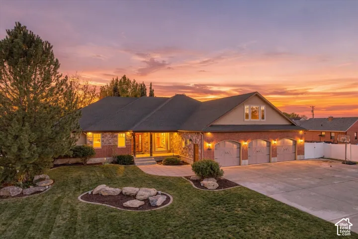Multi-level exterior featuring a combination of brick and stone veneer, an attached three-car garage, and hardscaped stone landscaping accents