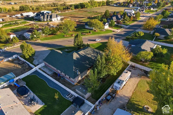 Aerial perspective featuring a residential lot with a fenced backyard, integrated concrete patio, mature trees, and a dedicated gravel side access area