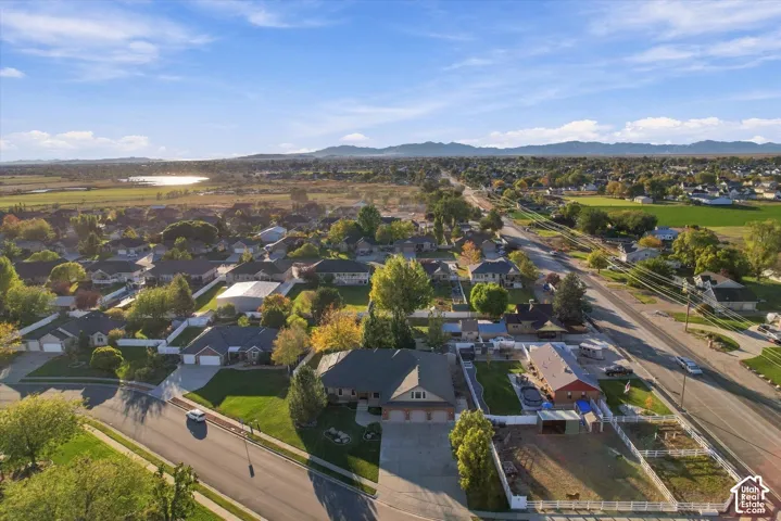 Aerial perspective featuring a multi-car garage, expansive driveway, fenced yard area, and a backdrop of mountain horizons