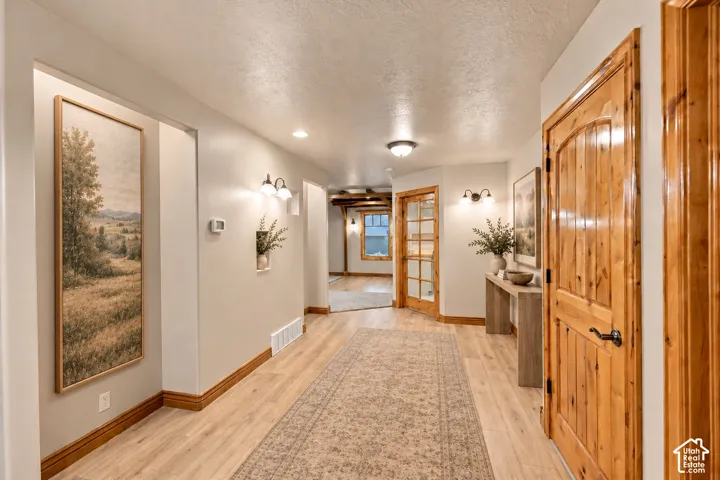 Interior hallway featuring wood-finish flooring, natural-finish wood door trim, recessed lighting, wall-mounted sconces, and built-in wall niches