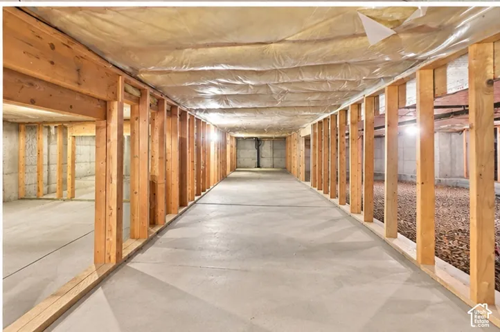 Unfinished basement area featuring poured concrete flooring, exposed wood stud framing, concrete foundation walls, and vapor barrier ceiling insulation