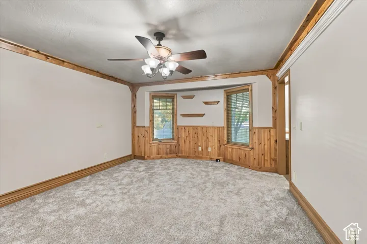 Room featuring wood wall paneling, crown molding, multi-pane windows, built-in shelving, and a ceiling fan with integrated lighting