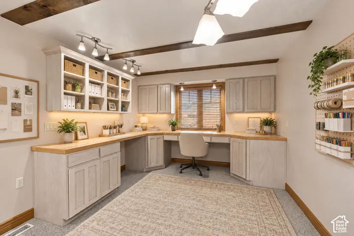 Built-in desk area with wood countertops, extensive cabinetry featuring under-cabinet lighting, open shelving, exposed ceiling beams, and integrated track lighting