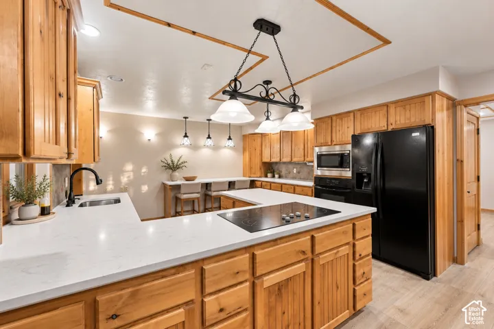 Kitchen featuring natural wood cabinetry, white stone-surface countertops, an integrated cooktop, a multi-light fixture over the island, and wood-finish flooring