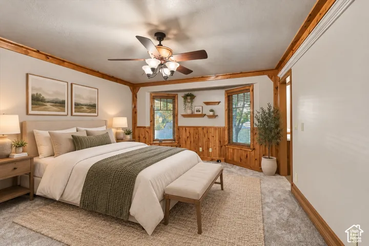 Wood wainscoting and crown molding, neutral carpeting, multi-light ceiling fan, and built-in wall shelving