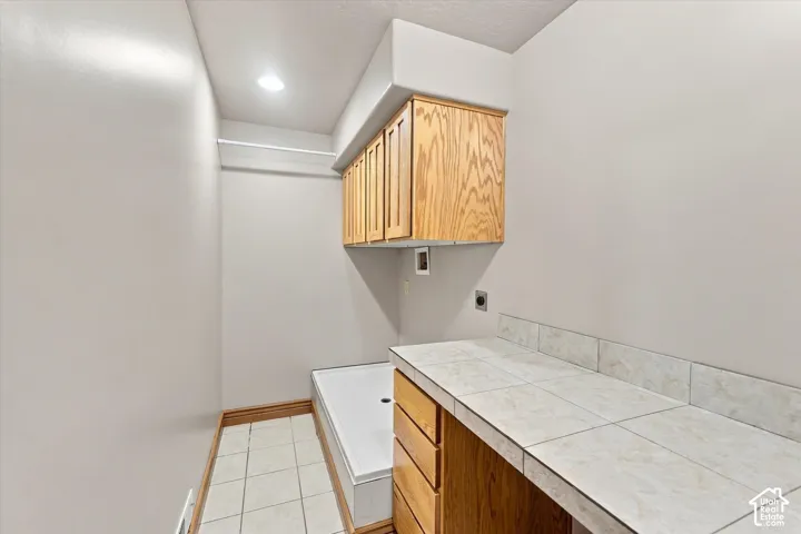 Utility space featuring tile flooring, built-in wooden cabinetry, a tiled countertop, and a ceiling-mounted light fixture