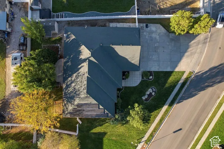 Aerial view of property featuring a large asphalt-shingle roof, integrated solar panels, concrete driveway, stone-bordered landscaping, and fenced grounds