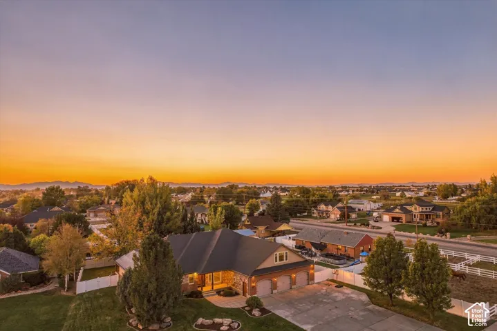 Aerial perspective of a multi-gabled residence featuring a three-car garage, stone masonry accents, paved driveway, and white vinyl perimeter fencing