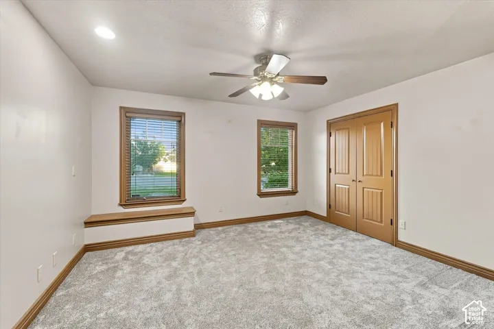Neutral interior space featuring wall-to-wall carpeting, dual-pane windows with integrated bench seating, solid wood-finish door trim, and a multi-light ceiling fan