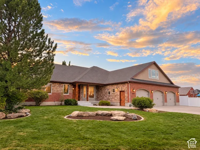 Brick and stone facade, three-car garage, pitched roofline, prominent front entry, and mature landscaping