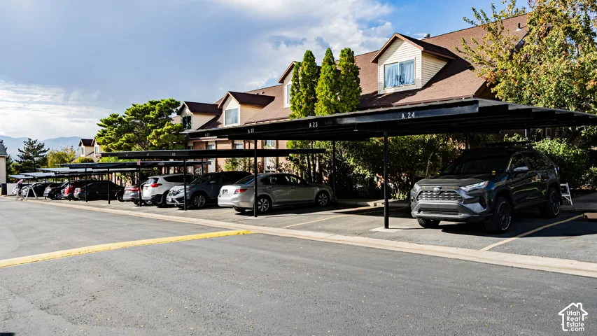 Covered parking spaces with asphalt paving and a building exterior featuring dormer windows