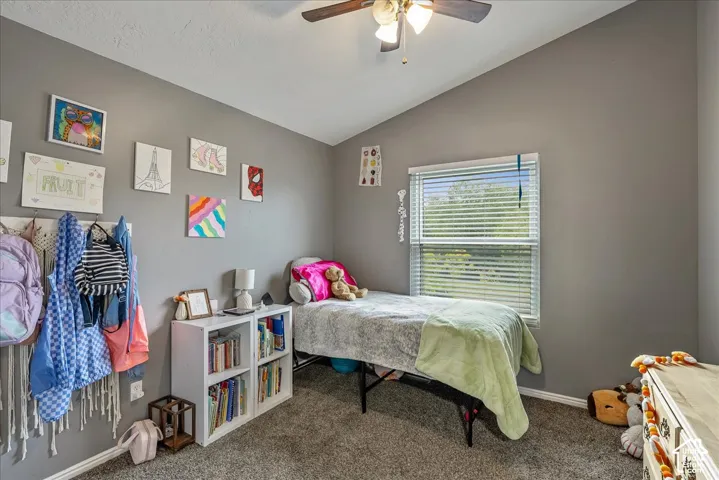 Vaulted ceiling room featuring neutral-tone walls, wall-to-wall carpeting, and a ceiling fan with integrated lighting