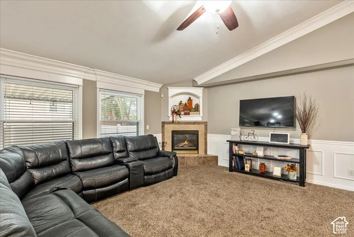 Vaulted ceiling with crown molding, corner fireplace featuring tile surround and built-in arched niche, and wall-mounted ceiling fan