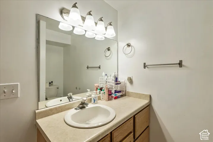 Bathroom vanity featuring a solid surface countertop with an integrated basin, wood cabinetry, wall-mounted mirror, and multi-bulb light fixture
