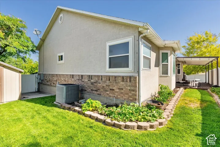 Stucco exterior with stone-veneer skirting, manicured lawn, stone-block garden border, and metal-frame patio structure