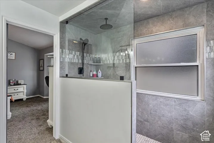 Walk-in shower featuring gray stone-finish wall tile, a frameless glass partition, a rainfall showerhead, and a mosaic tile shower floor