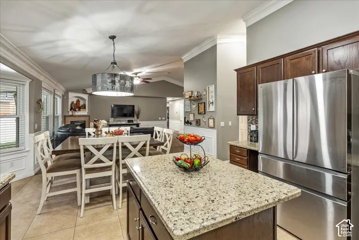 Kitchen featuring a central island with stone countertop, dark wood cabinetry, stainless steel refrigerator, tile flooring, and crown molding