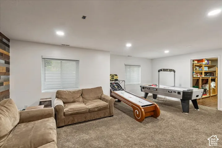Spacious room featuring neutral carpeting, recessed ceiling lighting, multi-toned wood-plank accent wall, and horizontal slat window blinds