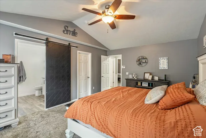 Vaulted ceilings, black sliding barn door, ceiling fan with integrated lighting, and multi-panel interior doors