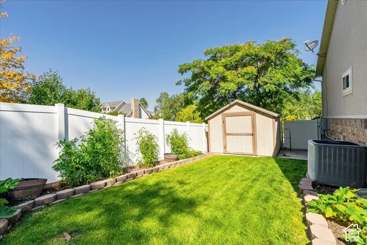 Backyard featuring a manicured lawn, white vinyl fencing, stone block edging, wonderful Garden and an outdoor storage shed.