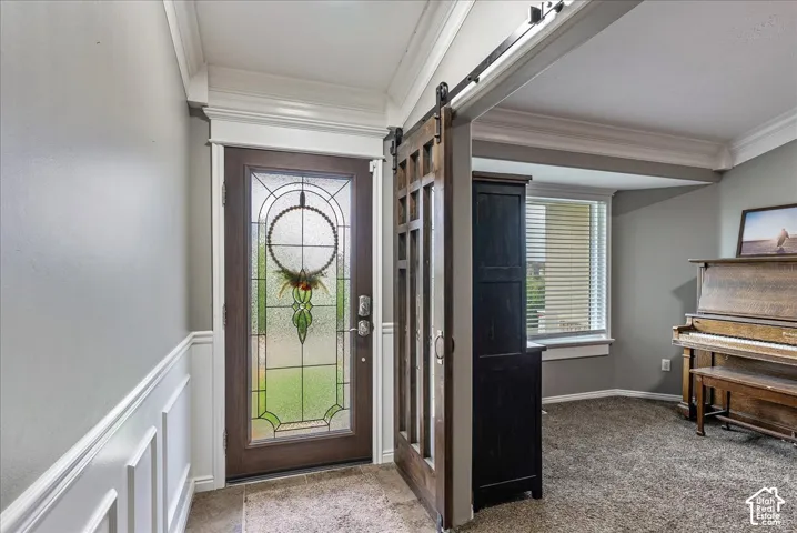 Entryway featuring an exterior door with decorative leaded glass, white wainscoting, crown molding, and a dark-finish wood sliding barn door