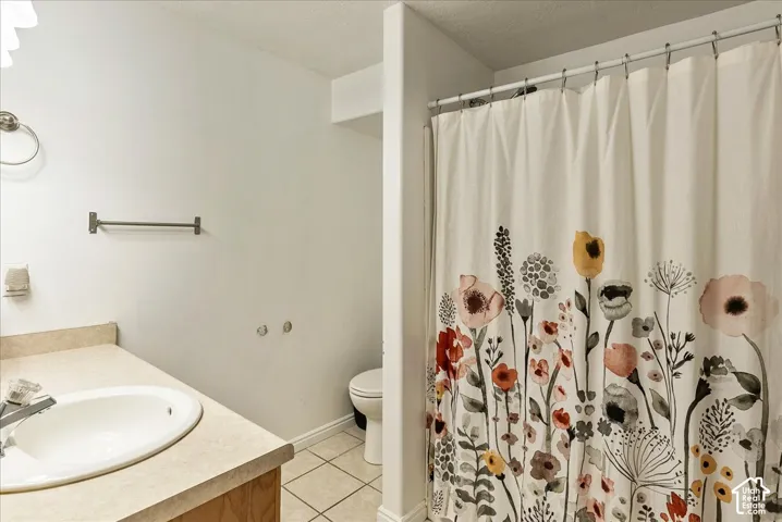 Bathroom featuring a vanity with an integrated oval sink, stone-finish countertop, tile flooring, and a shower area with a curtain rod
