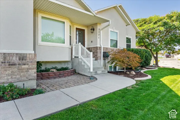 Welcoming front elevation featuring a raised entry with white railings, brick and stone exterior detailing, and manicured landscaping with mature plantings